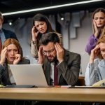 Professional office team experiencing emotional tension during a workplace meeting while a manager leads discussion in a modern business environment.