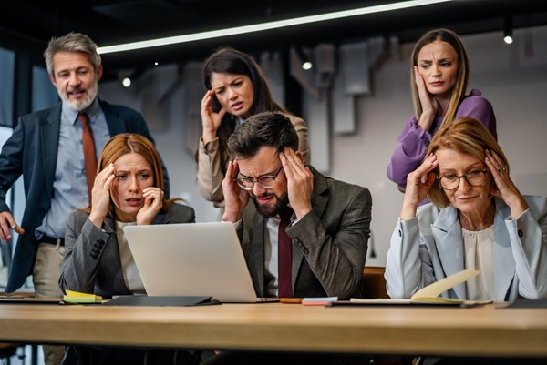 Professional office team experiencing emotional tension during a workplace meeting while a manager leads discussion in a modern business environment.