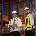 Seismic Requirements for Warehouse Racking and Industrial Facilities Professional engineers inspecting industrial warehouse racking systems and concrete slabs for seismic design compliance and structural safety.