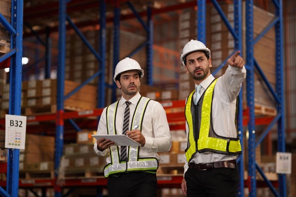Professional engineers inspecting industrial warehouse racking systems and concrete slabs for seismic design compliance and structural safety.